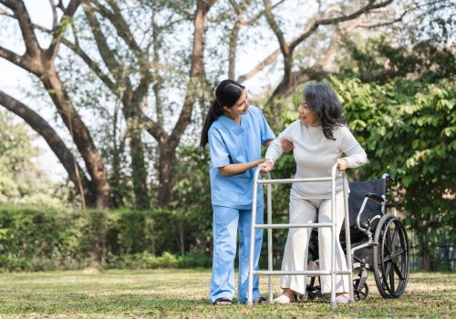 Elderly Woman with Caregiver Assisting in Rehabilitation Outdoors Using a Walker